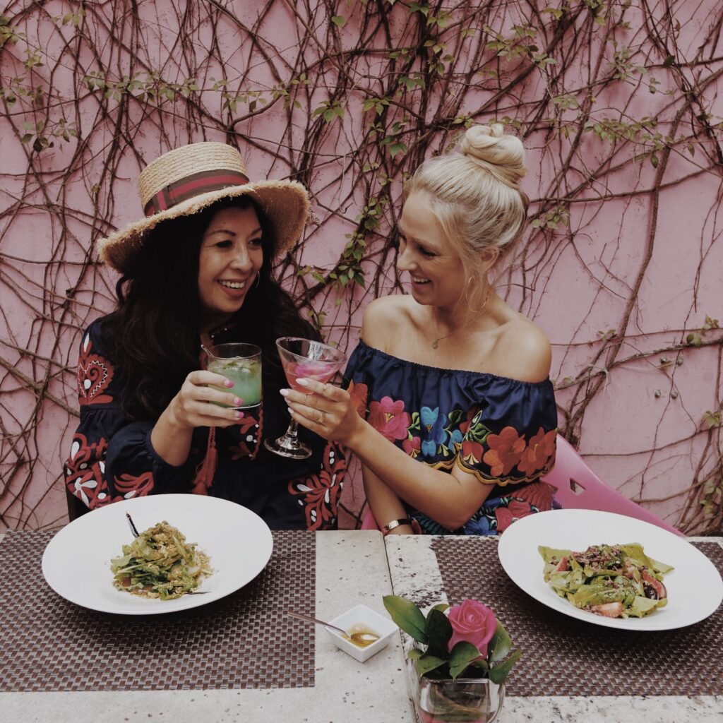 Two women toasting with colorful cocktails at a table in Mérida, Mexico.