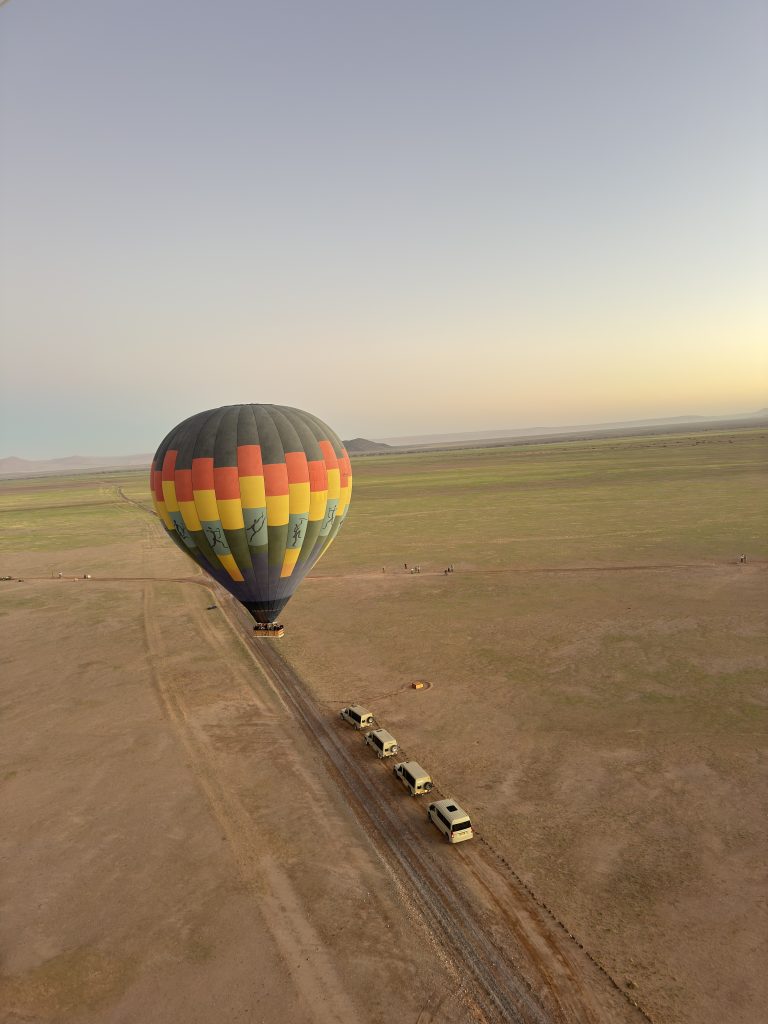 Hot air balloon over safari landscape with safari vehicles below.