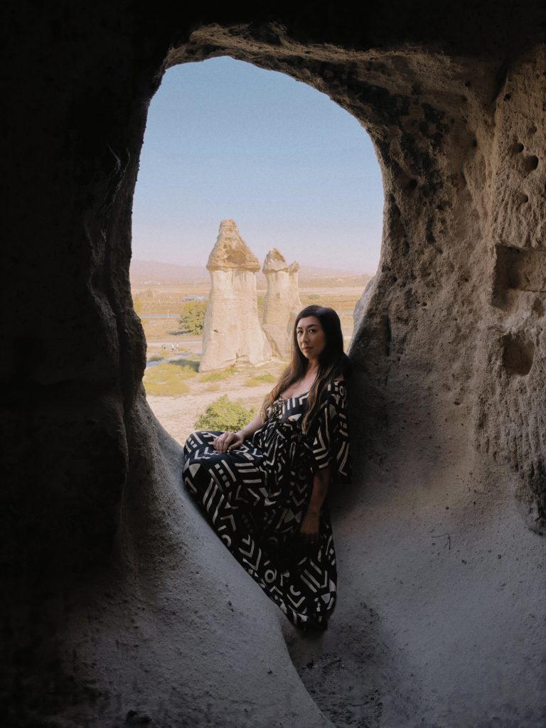 Woman in patterned dress sits in cave opening overlooking fairy chimneys in Cappadocia