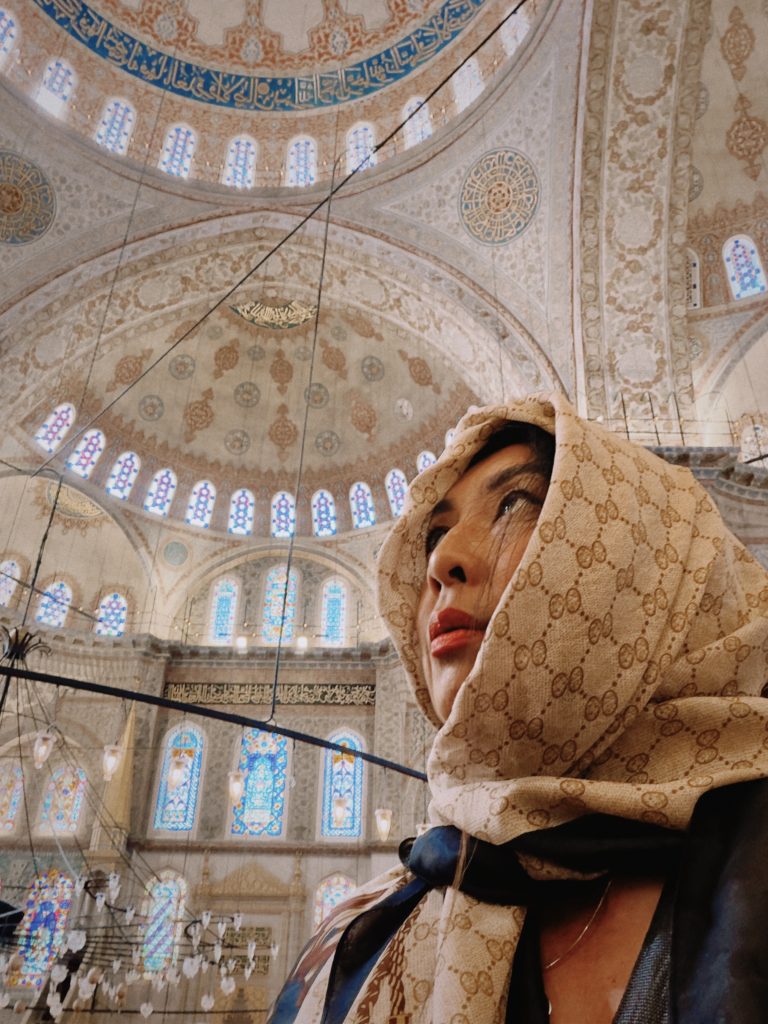 Betty in headscarf looking up inside a grand mosque with ornate dome and stained glass windows.